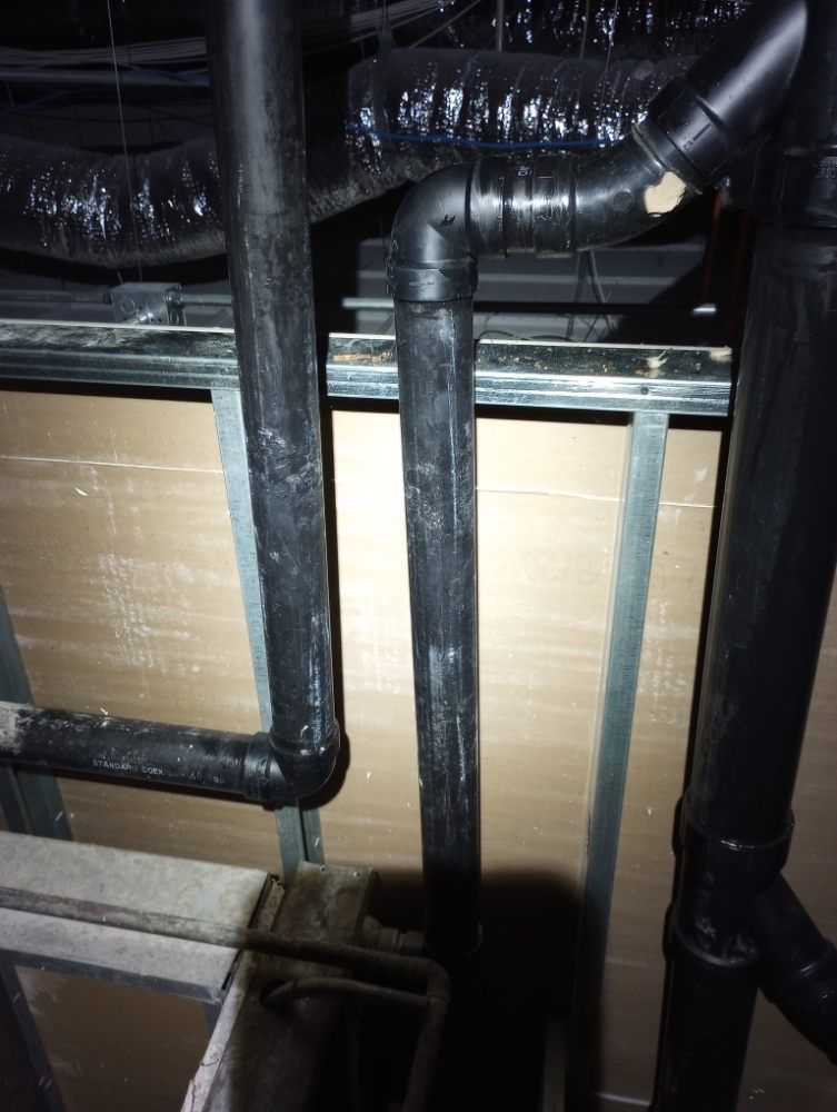 Black pipes and fittings attached to a ceiling with a metal framework.