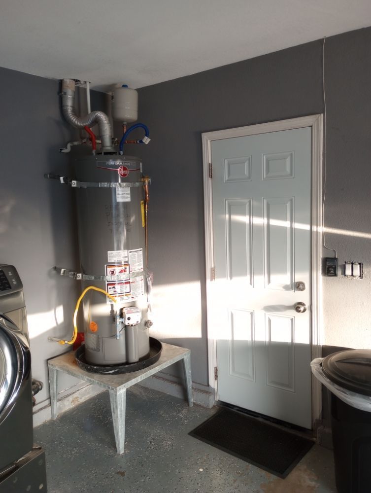 Water heater in a utility room. Gray tank, white door, and gray walls.