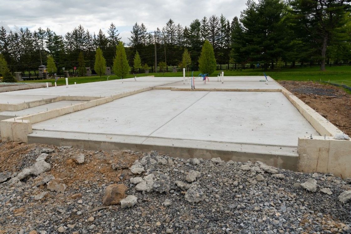 Concrete foundation of a building under construction. Grey concrete, dirt, and trees in the background.