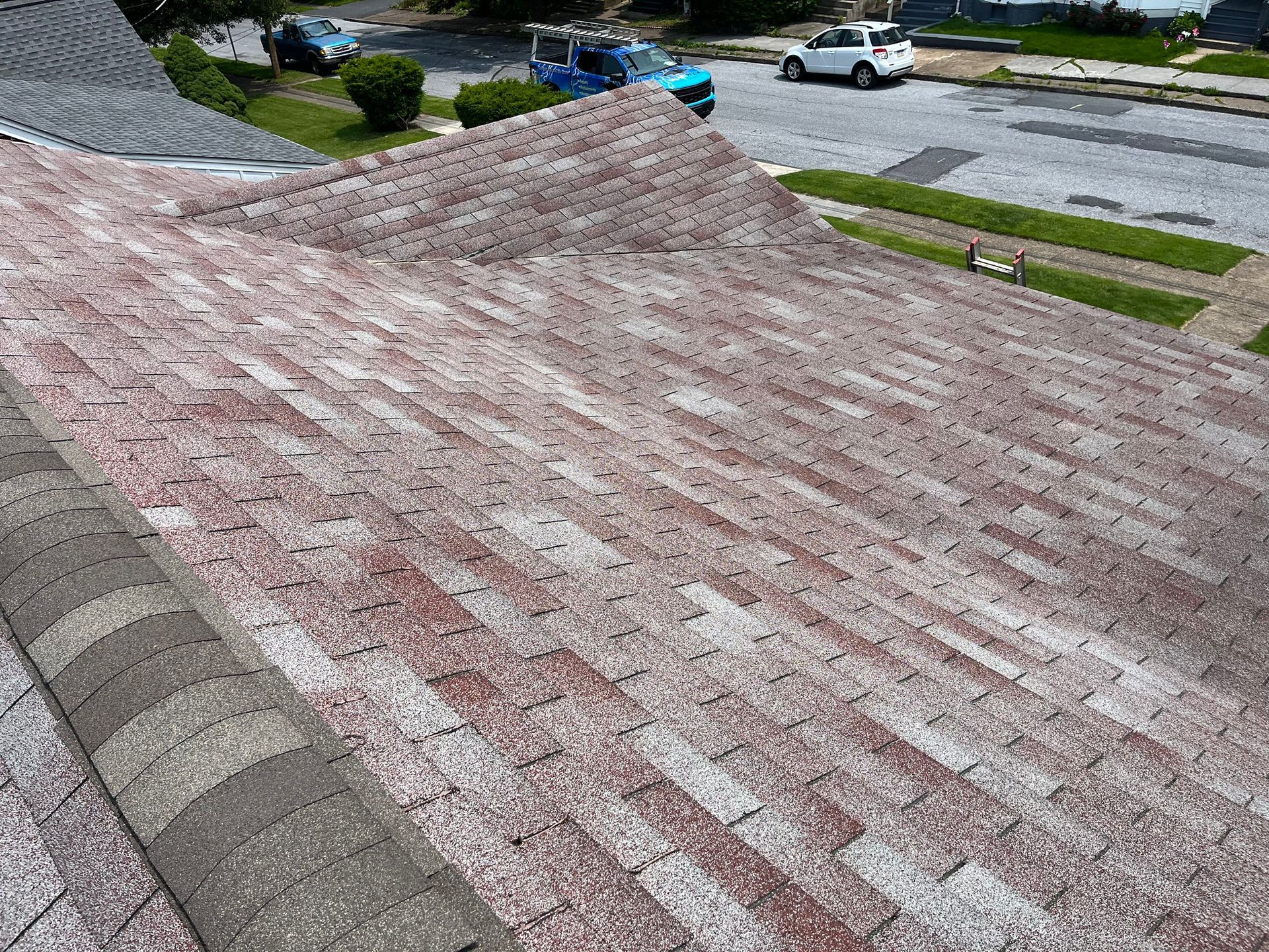 A high-angle view of a weathered residential shingle roof with reddish granules, showing signs of wear.