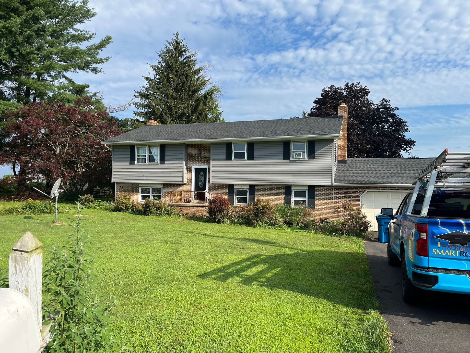 A two-story house with gray siding and stone veneer, with a blue service truck parked in the driveway on a sunny day.