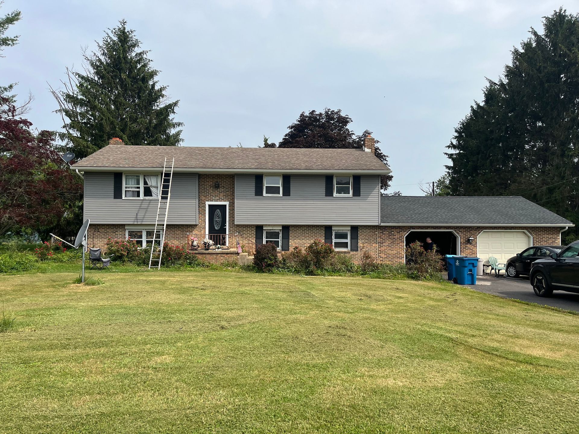 A split-level home with grey siding, stone accents, and an attached garage, set behind a green lawn under a cloudy sky.