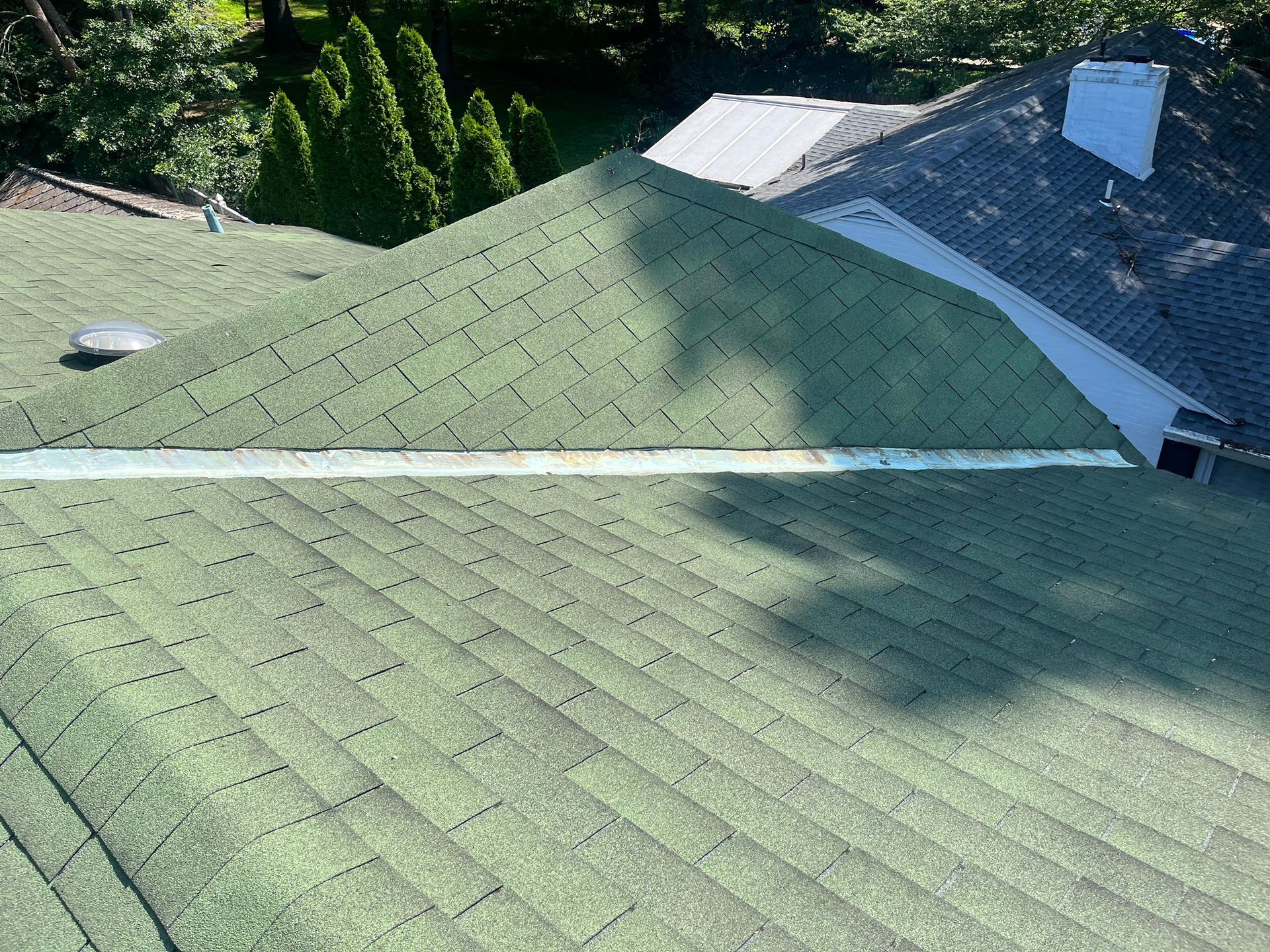 An angled view of a green shingled roof featuring a long, light-colored metal flashing strip running across the slope.