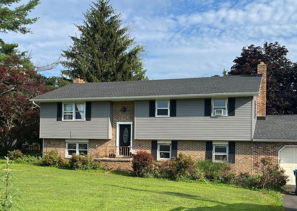 A two-story house with gray siding and stone veneer, with a blue service truck parked in the driveway on a sunny day.