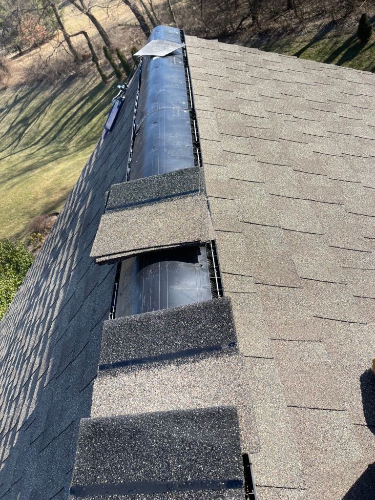 A close-up of a house roof showing partially installed shingles over a black underlayment along the ridge.