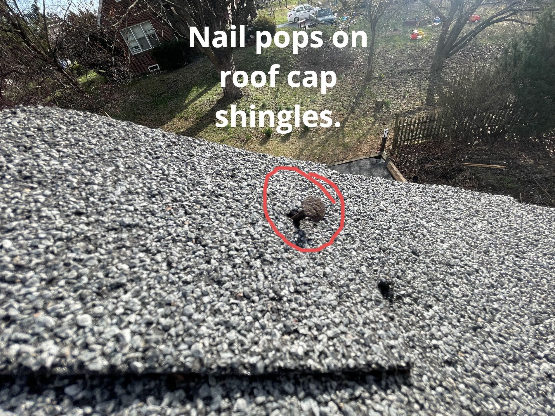 A close-up view of a shingled roof ridge with a red circle highlighting a protruding nail head, labeled a nail pop.