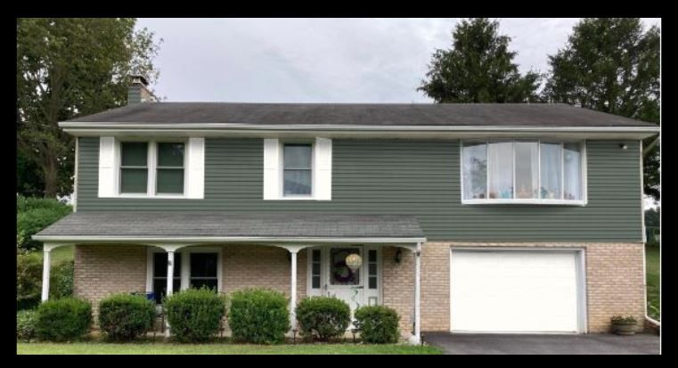 A two-story house with green horizontal siding on the top floor, brick on the bottom, a garage, and a covered front porch.