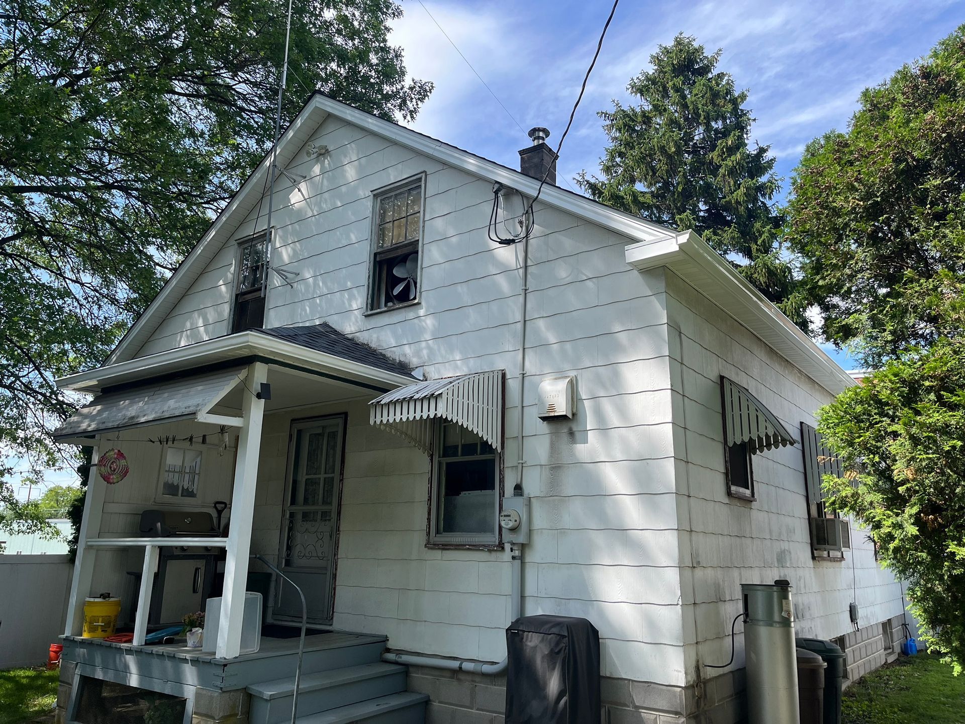 A white two-story house with a small front porch, metal window awnings, and an outdoor fireplace chimney.