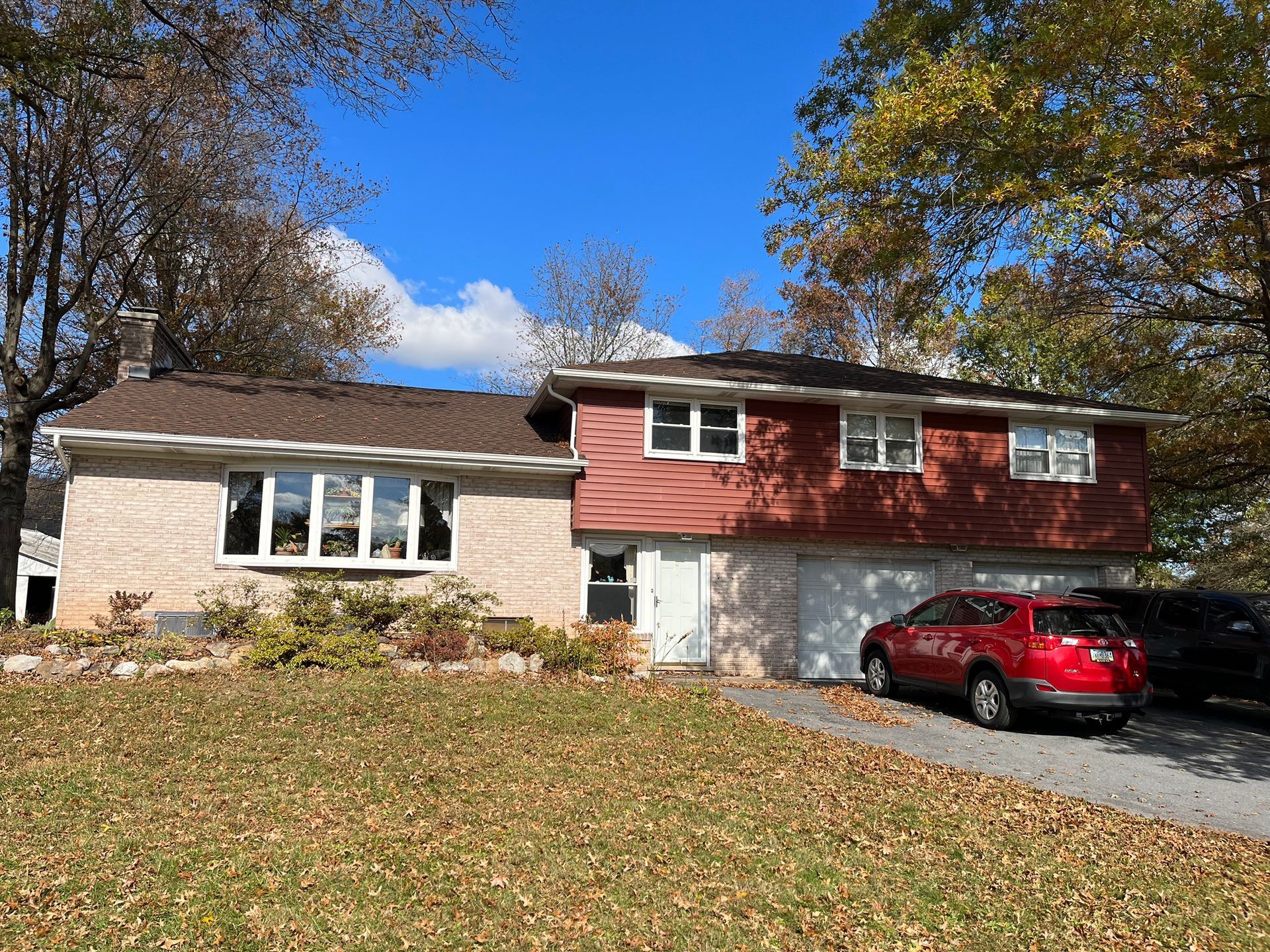A split-level house with a red upper level, a brick lower level, a garage, and a driveway with a red car.