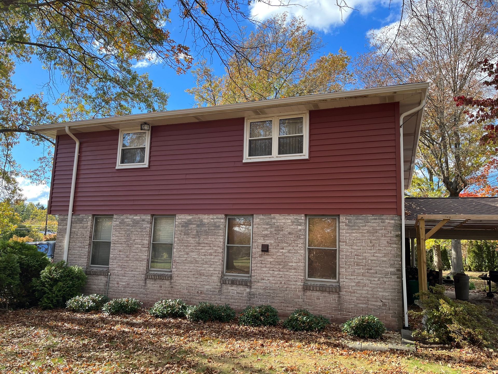 A two-story house with red horizontal siding on the top level and a light-colored brick exterior on the bottom level.