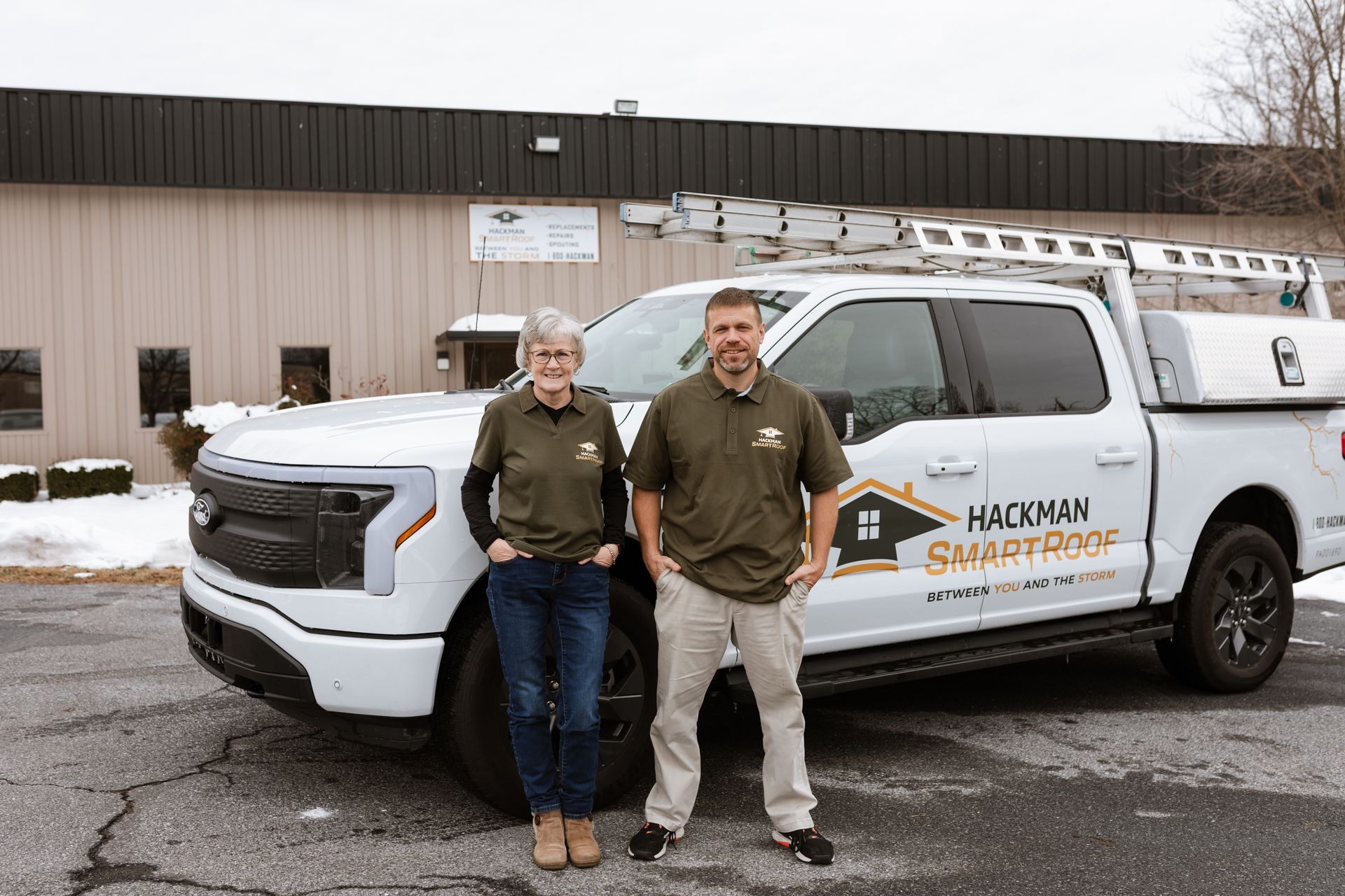 Two people stand in front of a white Ford pickup truck with a 