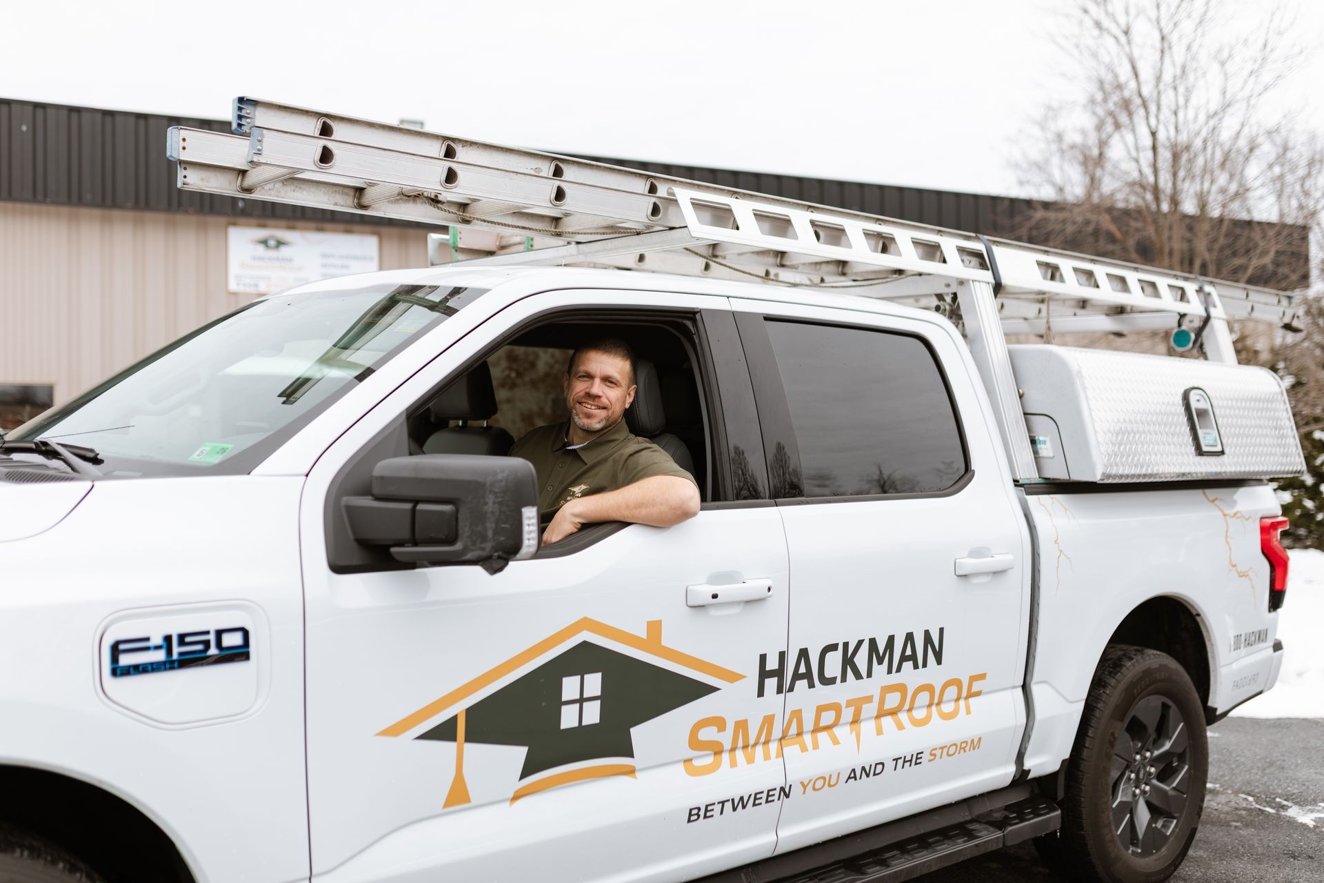 A man sits in the driver’s seat of a white pickup truck labeled 