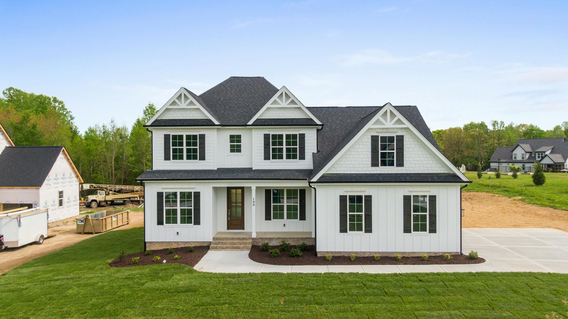 A white, two-story house with a black shingled roof, dark window shutters, and a front porch, set on a grassy lawn.
