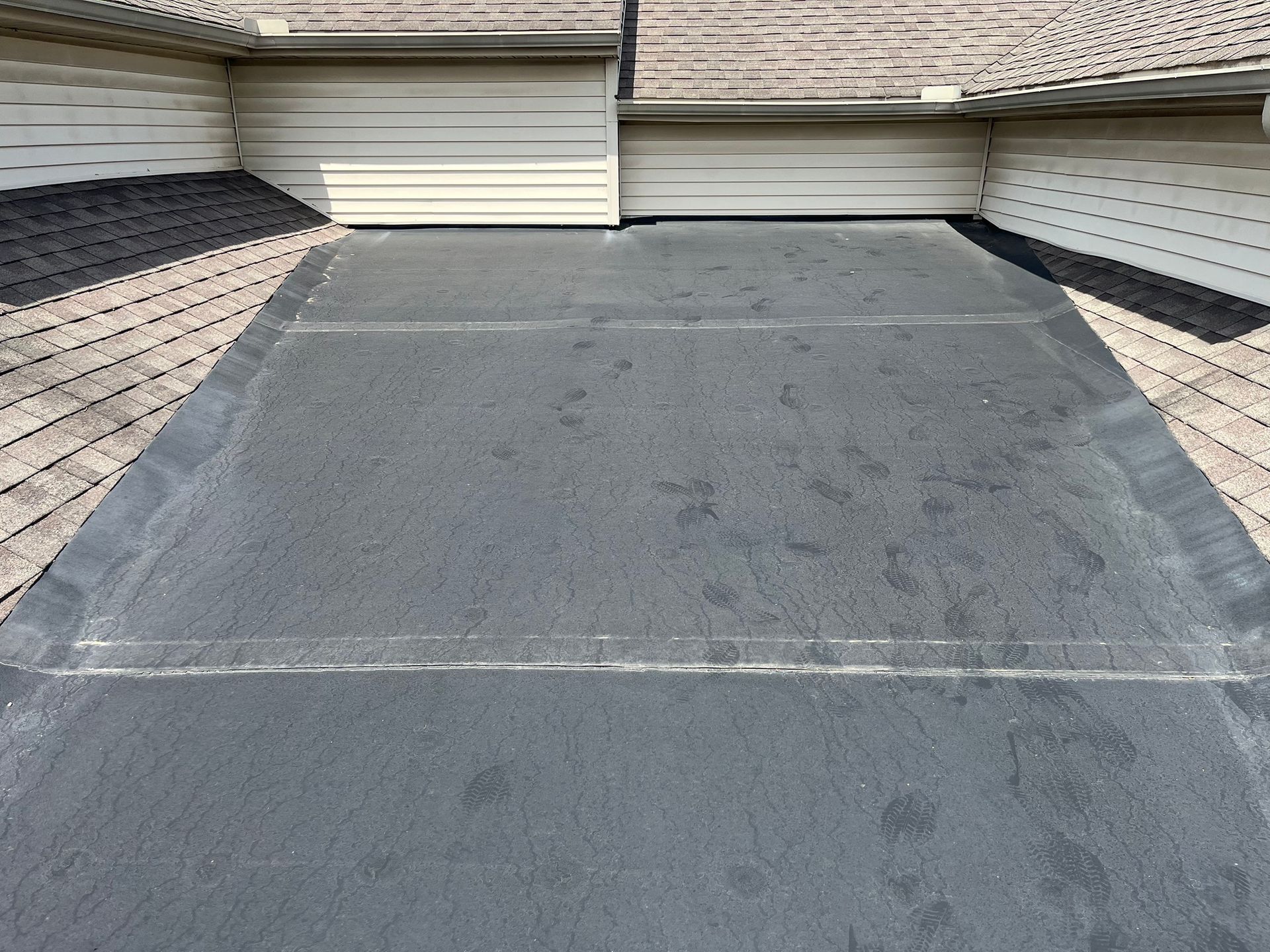 A construction worker installs black waterproof roofing membrane on a flat roof under a blue sky.