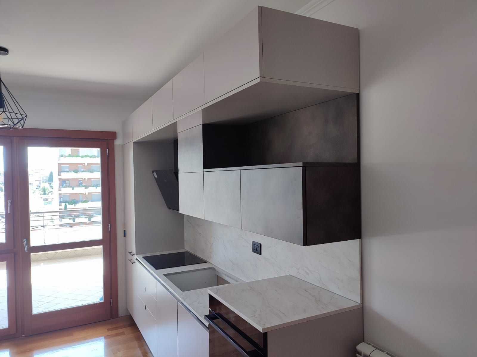 Cucina moderna con mobili chiari e cappa scura, vicino alla porta-finestra del balcone.