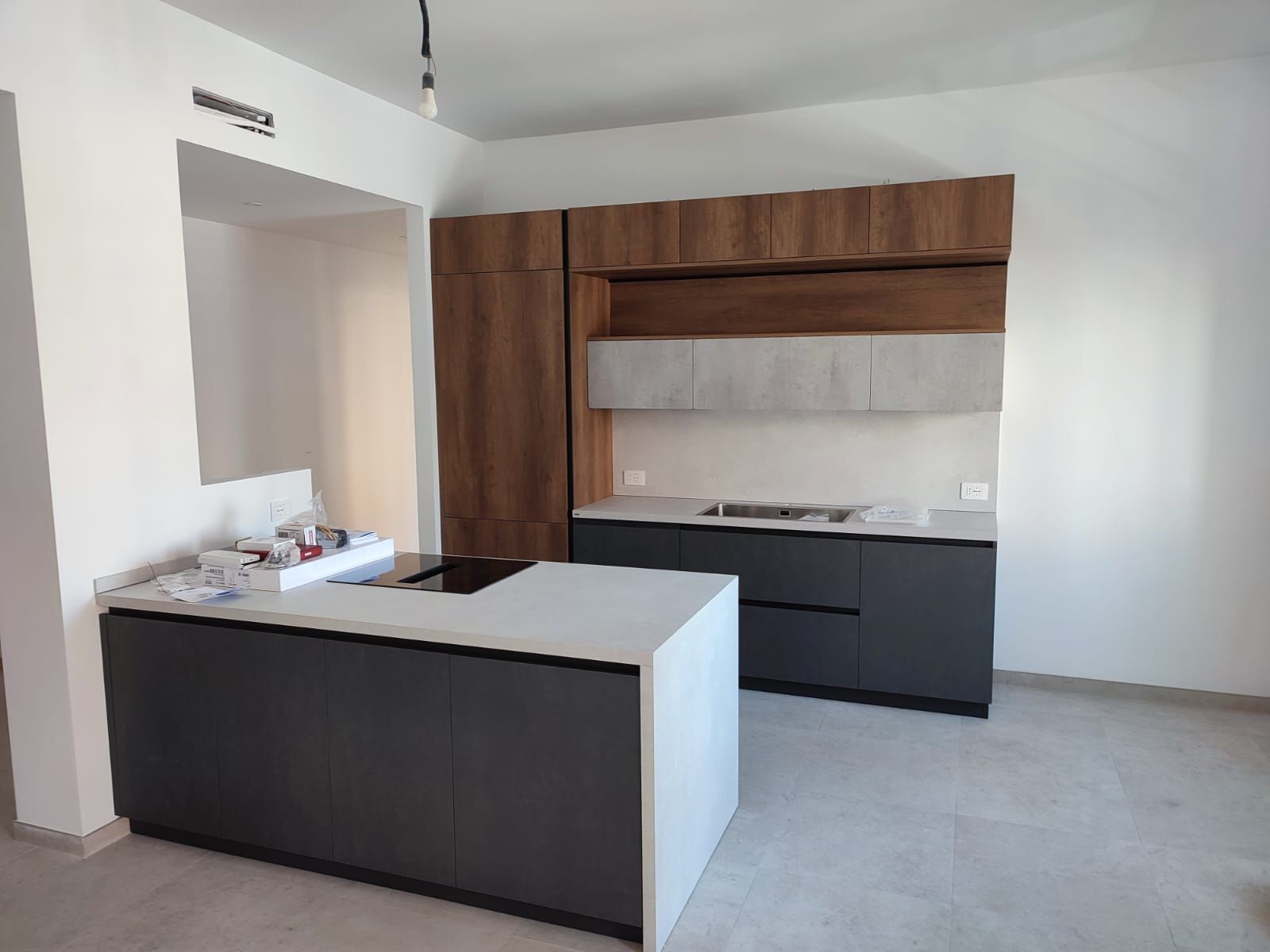 Cucina moderna con mobili grigi e in legno, isola con piano di lavoro bianco e pareti bianche.