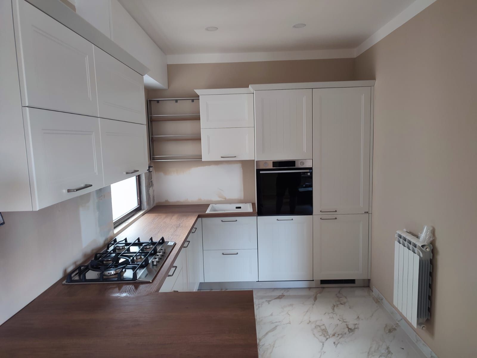 Una cucina con mobili bianchi, un piano di lavoro in legno e una stufa. Le pareti sono beige.