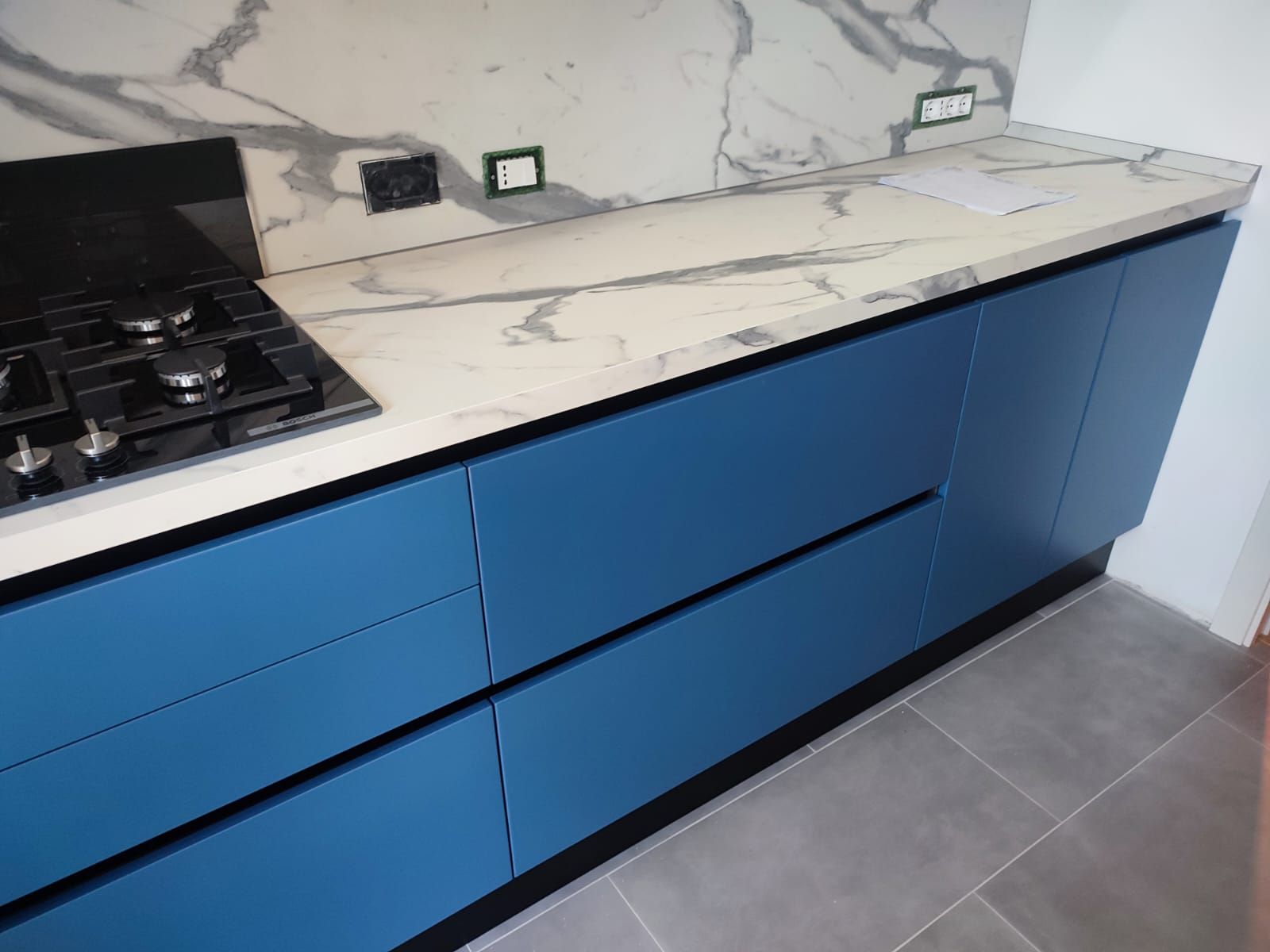 Mobili da cucina blu con piano di lavoro e paraschizzi in marmo bianco.