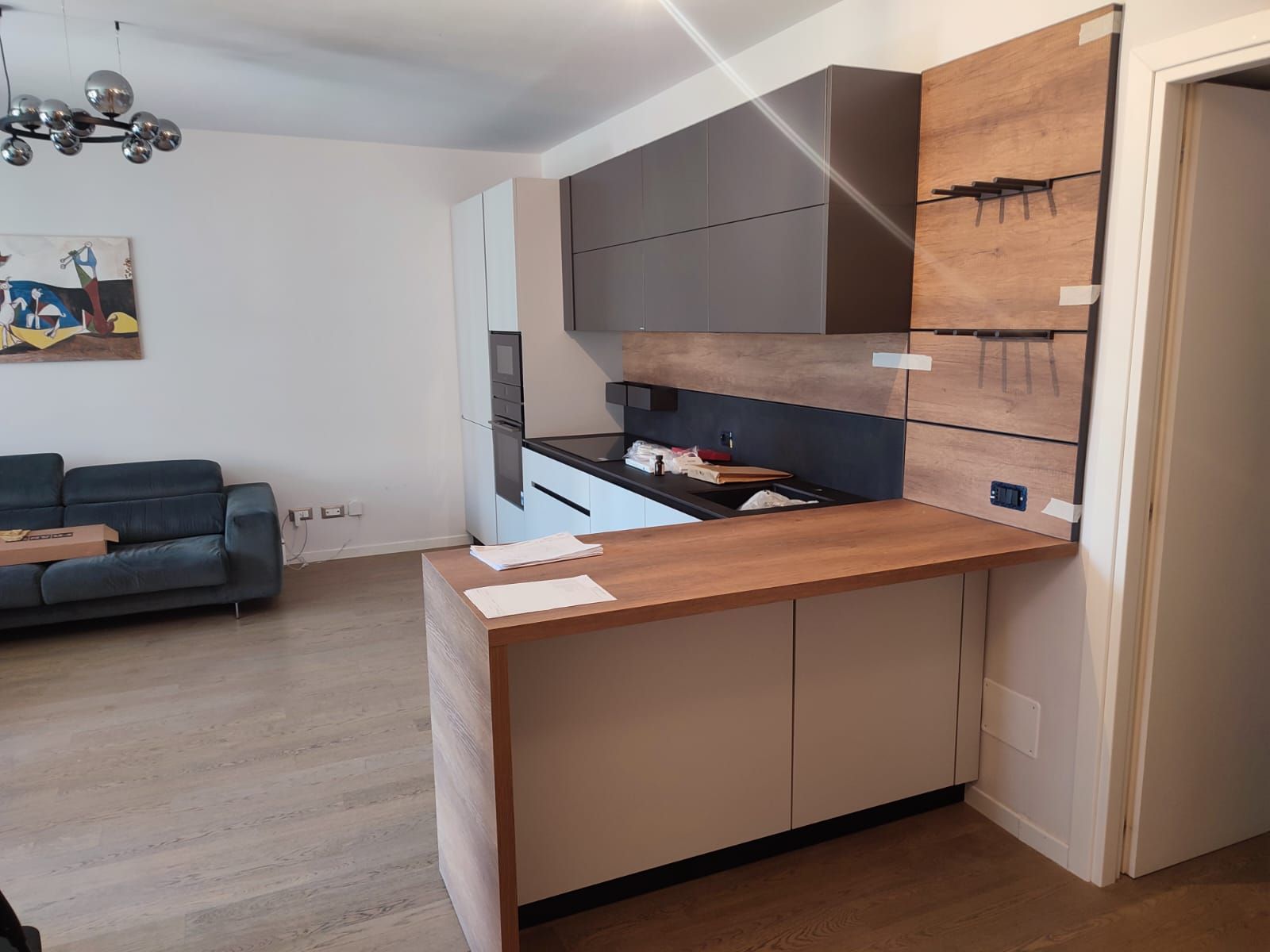 Cucina moderna con isola in legno chiaro e mobili grigi, adiacente al soggiorno.