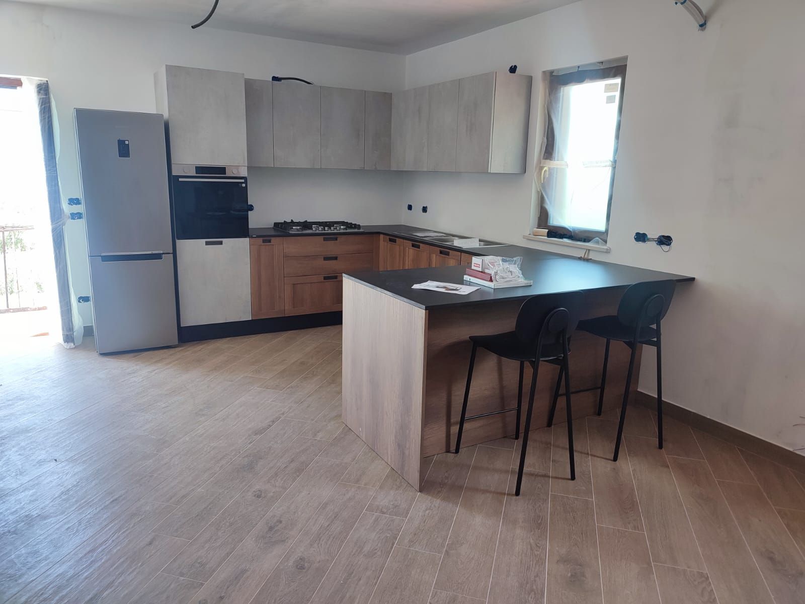 Cucina moderna con mobili in legno chiaro, isola nera e frigorifero.