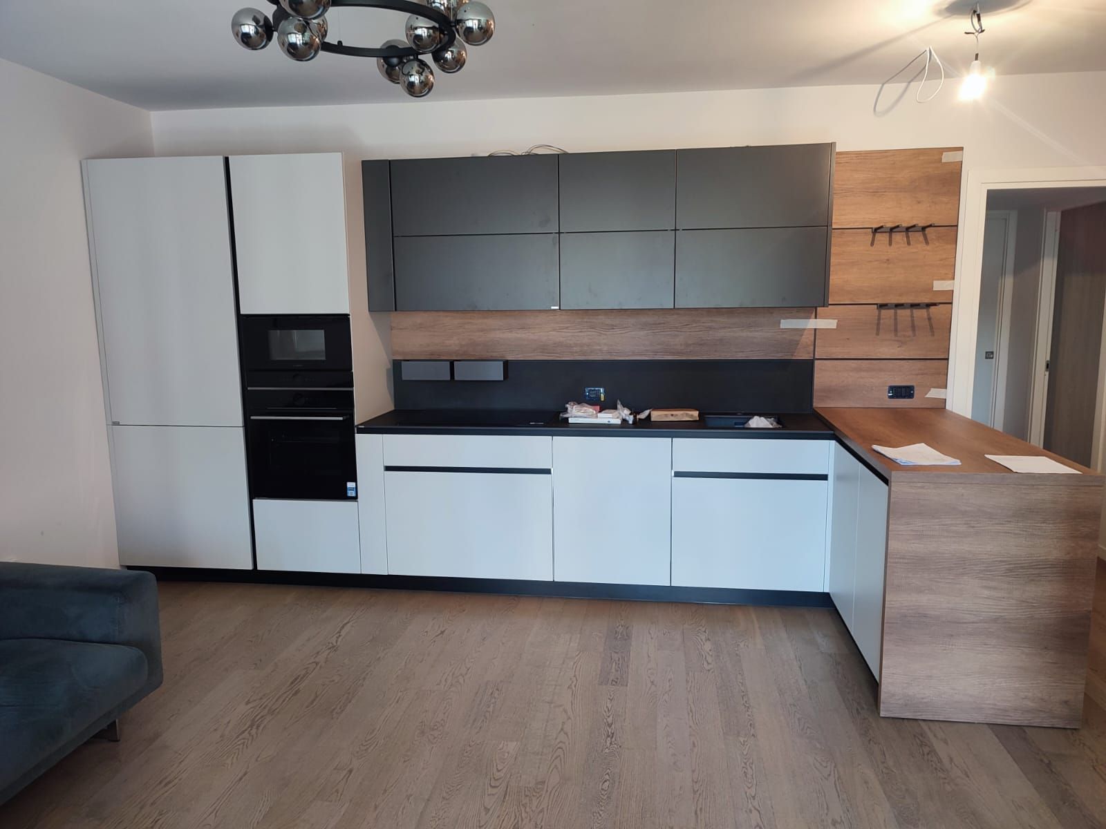 Cucina moderna con mobili bianchi e neri, dettagli in legno ed elettrodomestici da incasso.