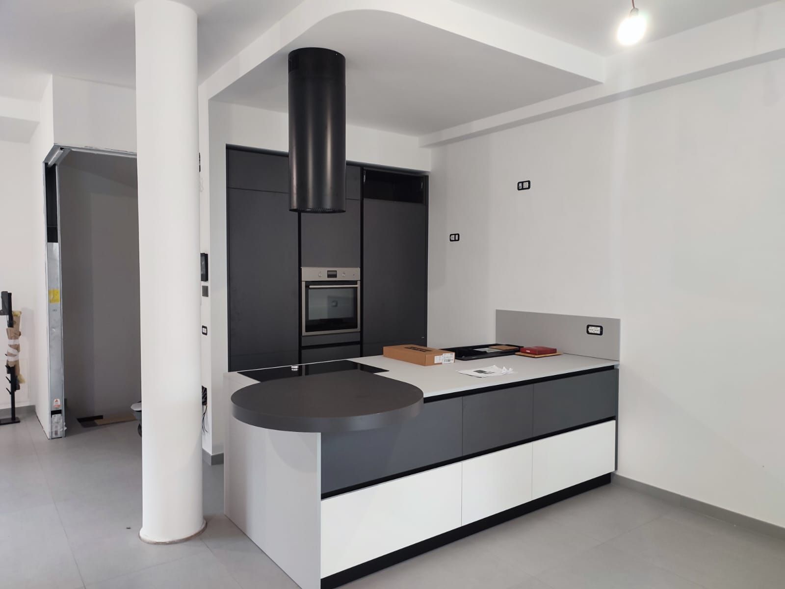 Cucina moderna grigia e bianca con isola, forno, cappa aspirante e piano di lavoro rotondo.