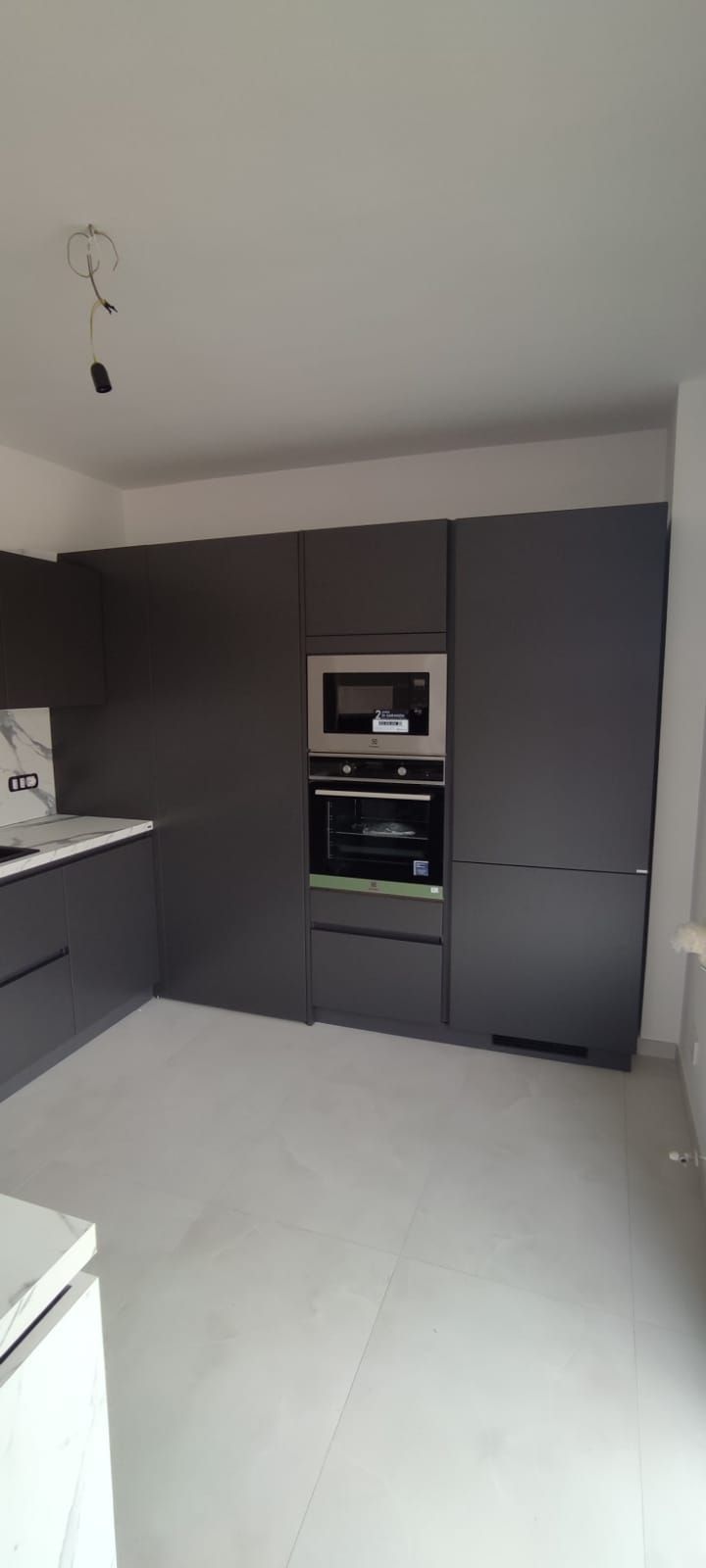 Mobili da cucina grigio scuro con forno e microonde integrati. Pavimento grigio chiaro e pareti bianche.