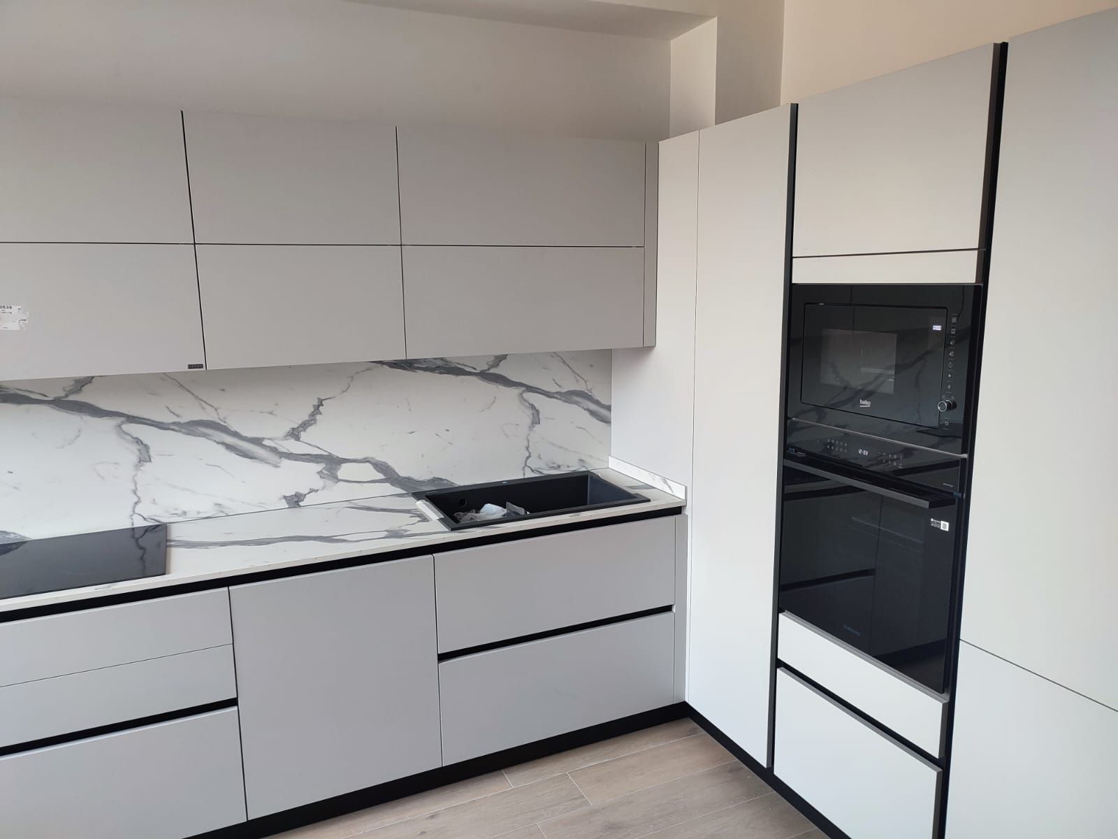 Moderna cucina bianca con finiture nere e paraschizzi in marmo.