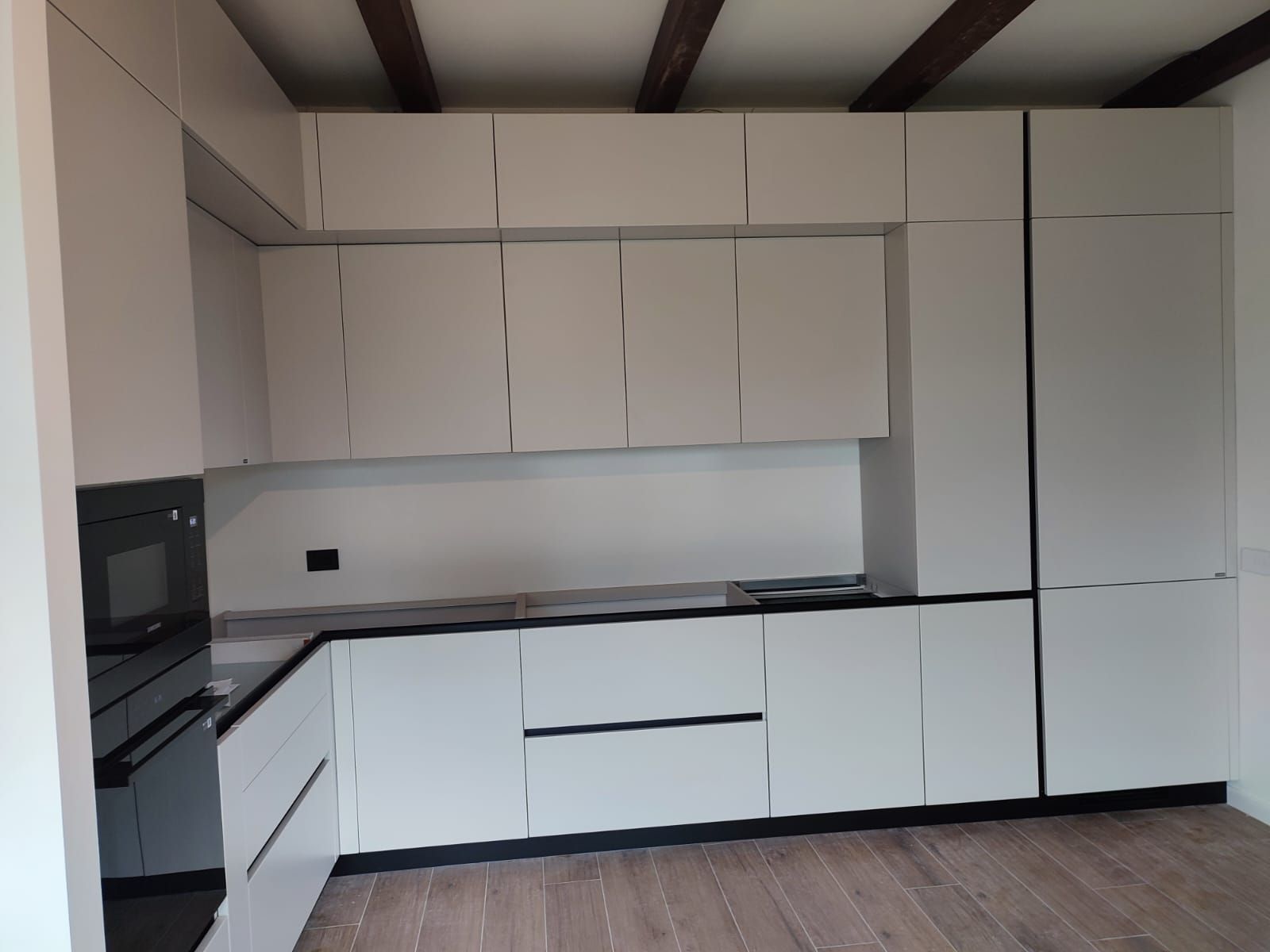 Moderna cucina bianca con dettagli neri, dotata di mobili, elettrodomestici e travi in legno sul soffitto.