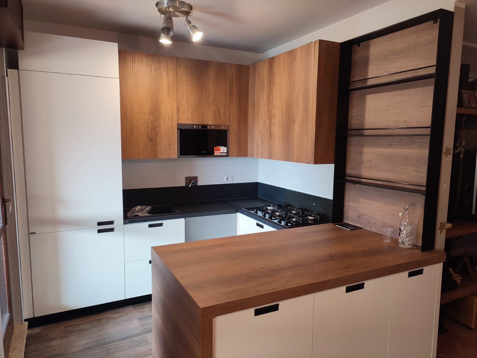 Cucina moderna con mobili bianchi e in legno, ripiani neri e un'isola centrale con piano cottura.