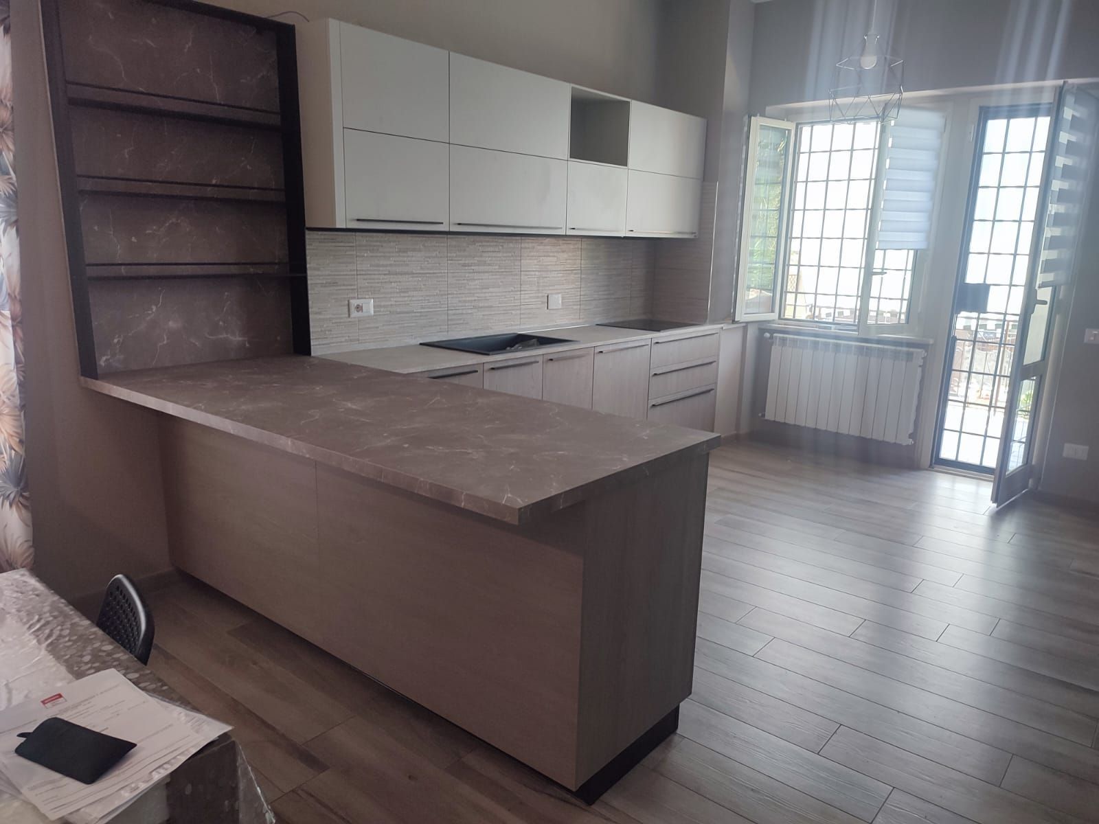 Cucina moderna con isola e mobili dai colori chiari, piano cottura incorporato e finestra.