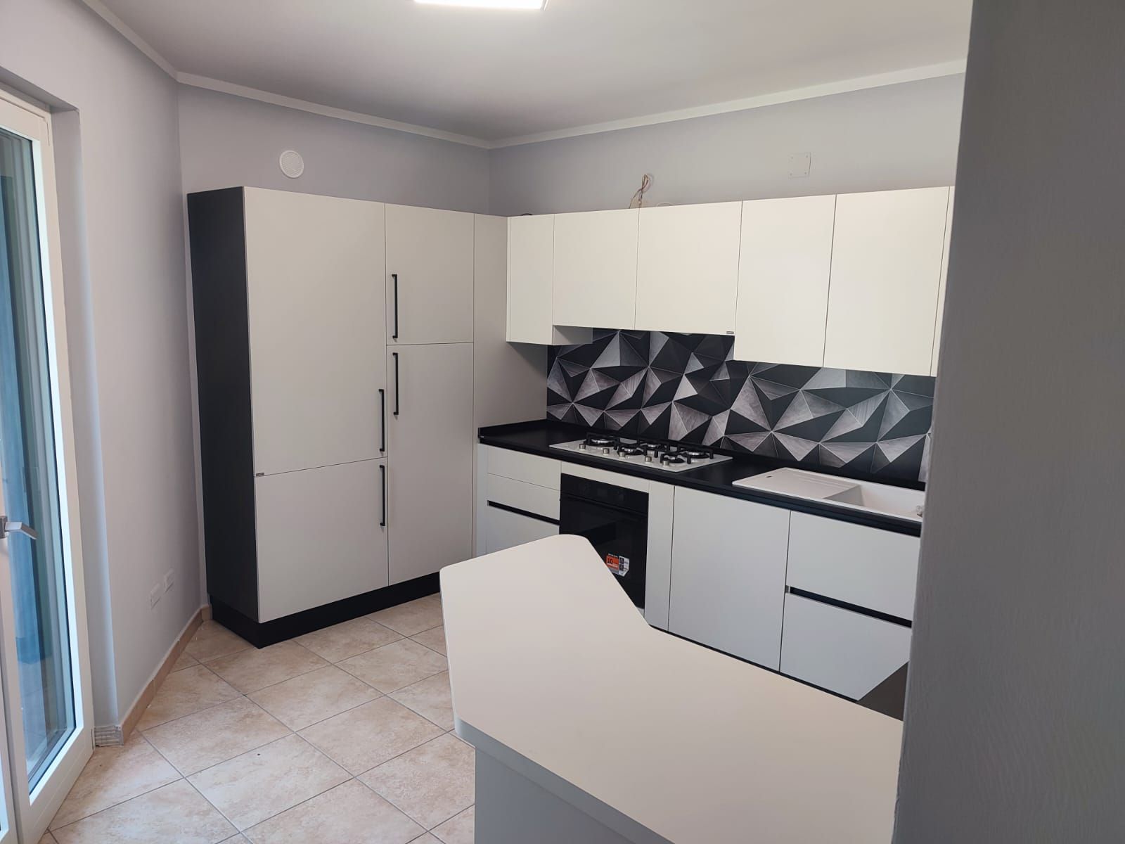 Cucina moderna con mobili bianchi, paraschizzi nero e piano di lavoro bianco.