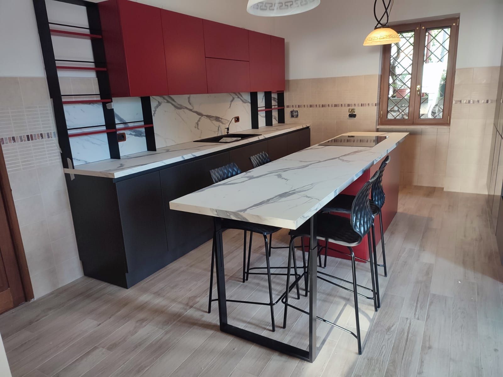 Cucina moderna con mobili rossi, isola lunga e sgabelli in metallo nero.