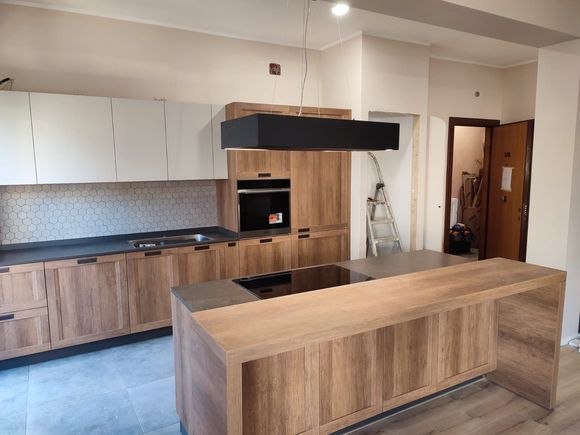 Cucina moderna con mobili in legno, isola e cappa nera; è visibile una porta.