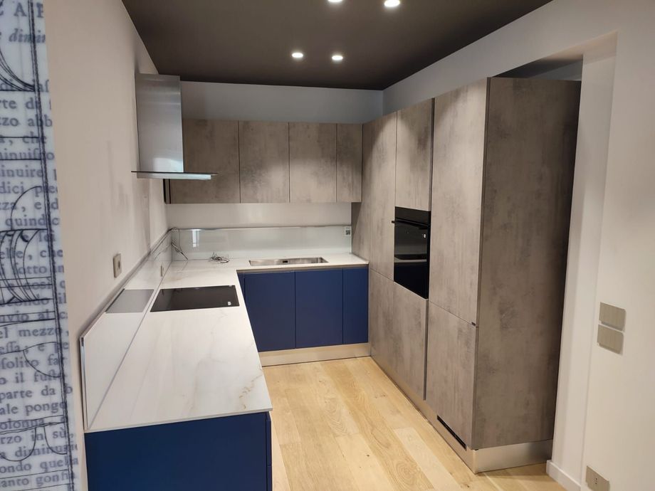 Cucina moderna con mobili grigi, mobili base blu e pavimento in legno chiaro.