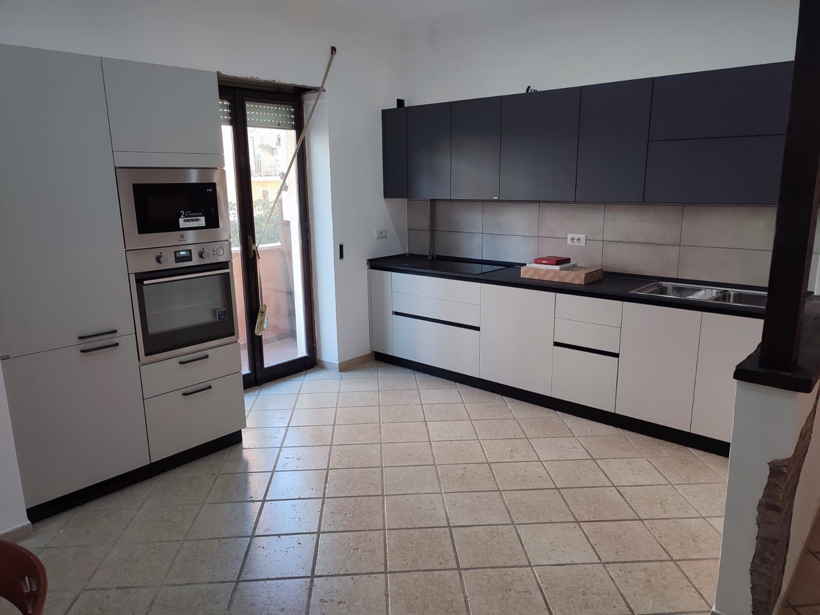 Cucina moderna con mobili grigi e bianchi, ripiani neri e pavimento piastrellato.
