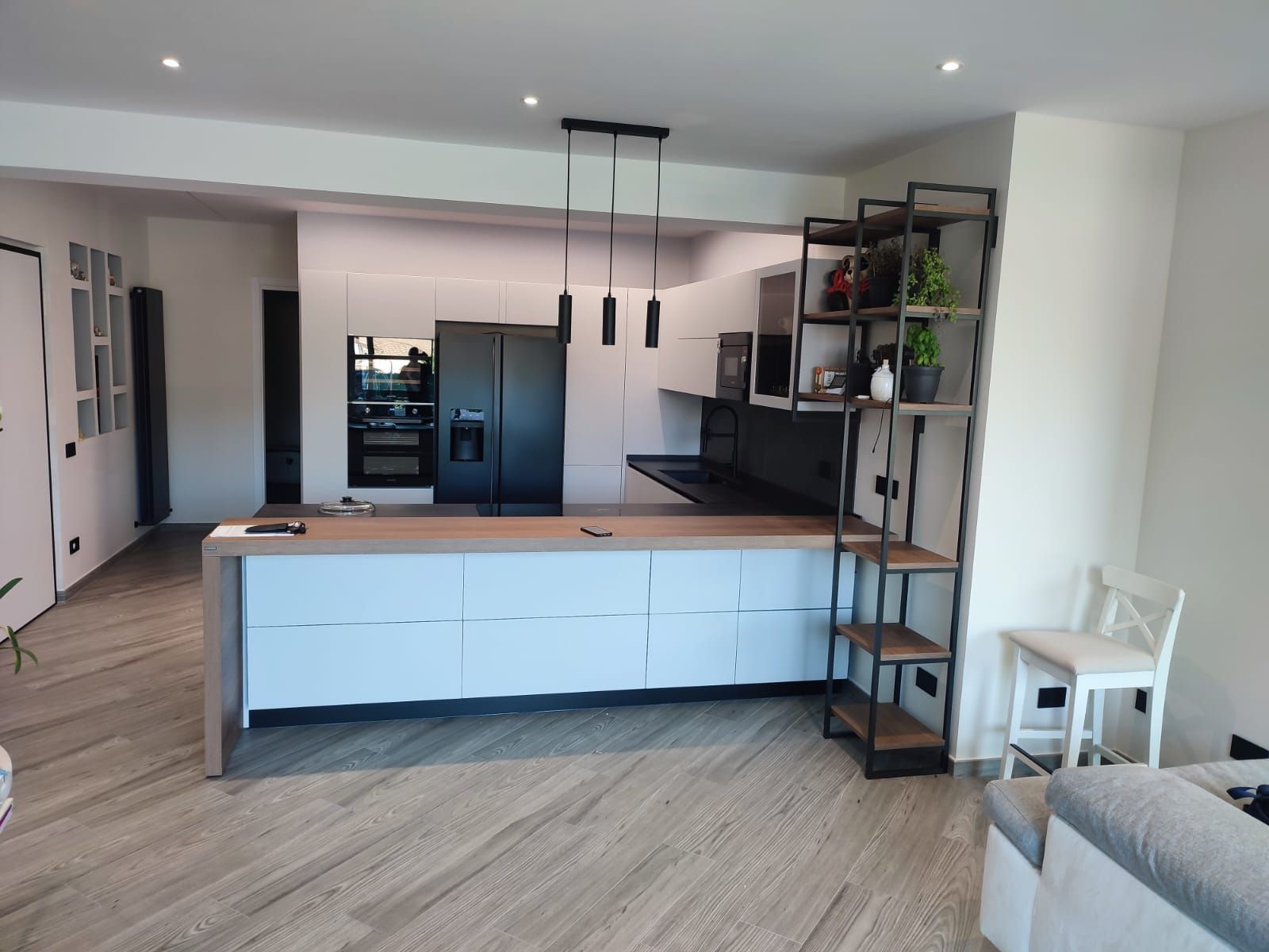 Cucina moderna con mobili bianchi, piano di lavoro in legno, dettagli neri e scaffalature in metallo.