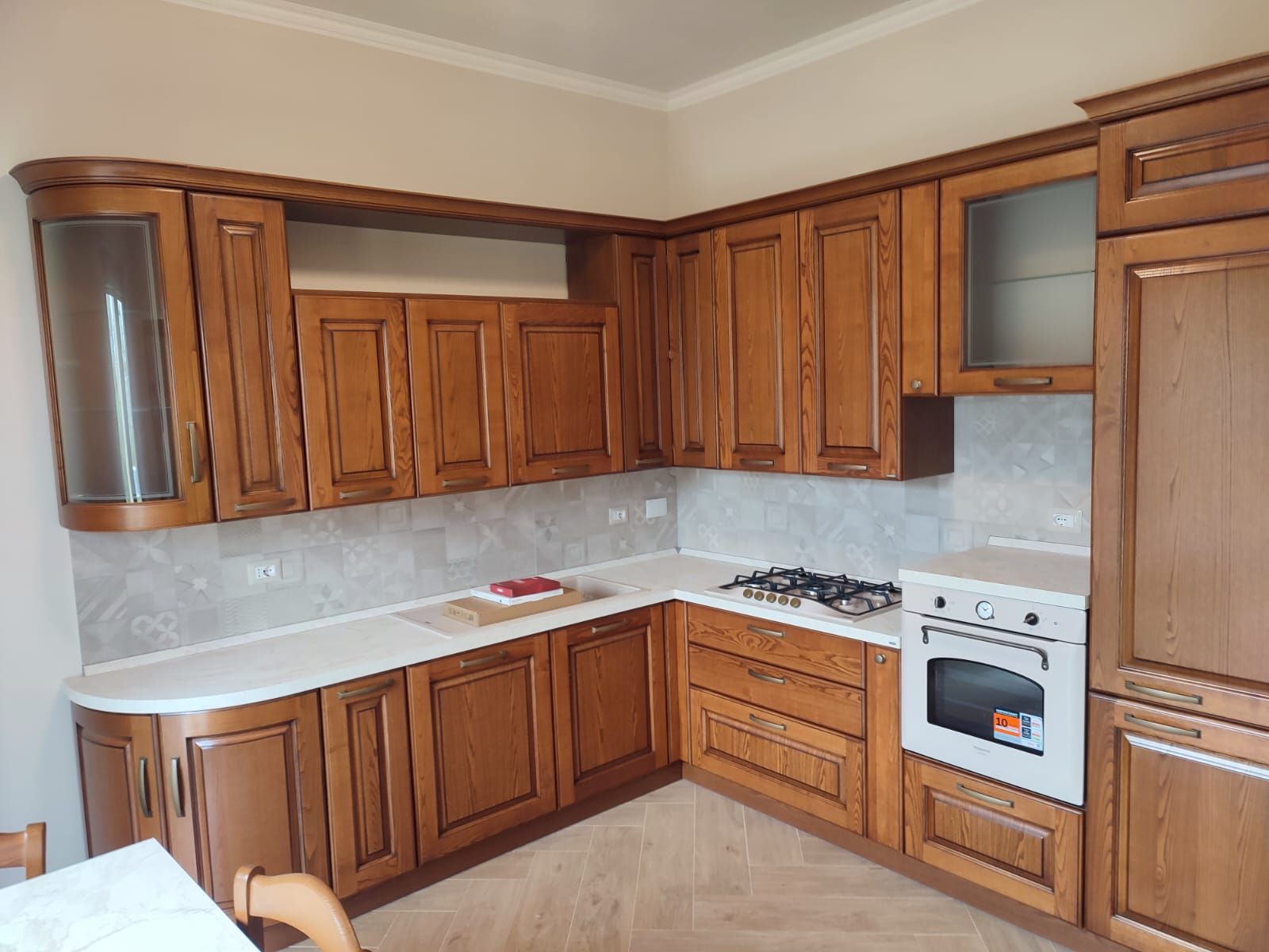 Mobili da cucina in legno con piano di lavoro bianco, paraschizzi grigio chiaro e fornello a gas.
