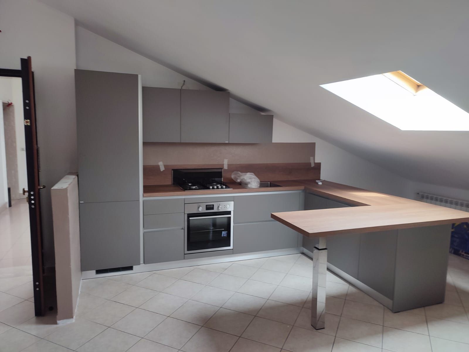 Cucina grigia con piano di lavoro in legno in una stanza con soffitto spiovente e lucernario.