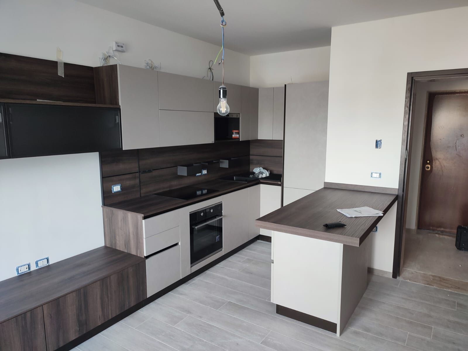 Cucina moderna con mobili bicolore, elettrodomestici neri, bancone per la colazione e pavimenti in legno chiaro.