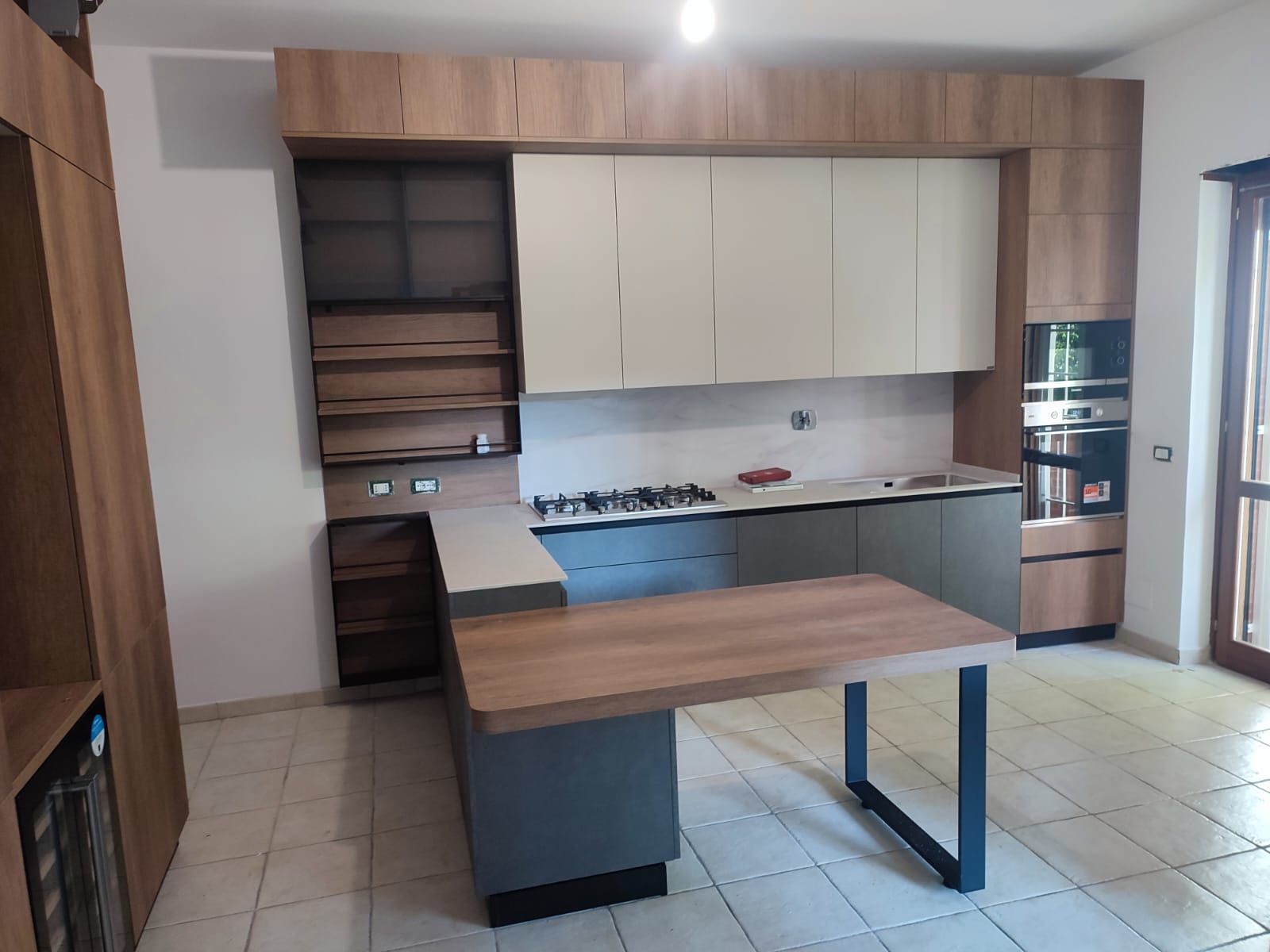 Cucina moderna con mobili in legno chiaro e grigi, isola grigia e ripiani beige.