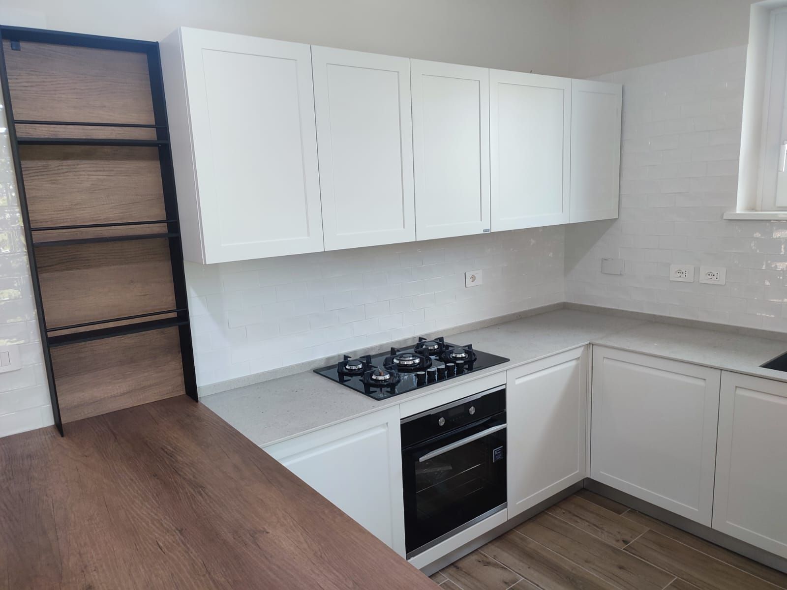 Cucina bianca con mobili, piano di lavoro, forno e piano cottura integrati. Ripiani e pavimento in legno.