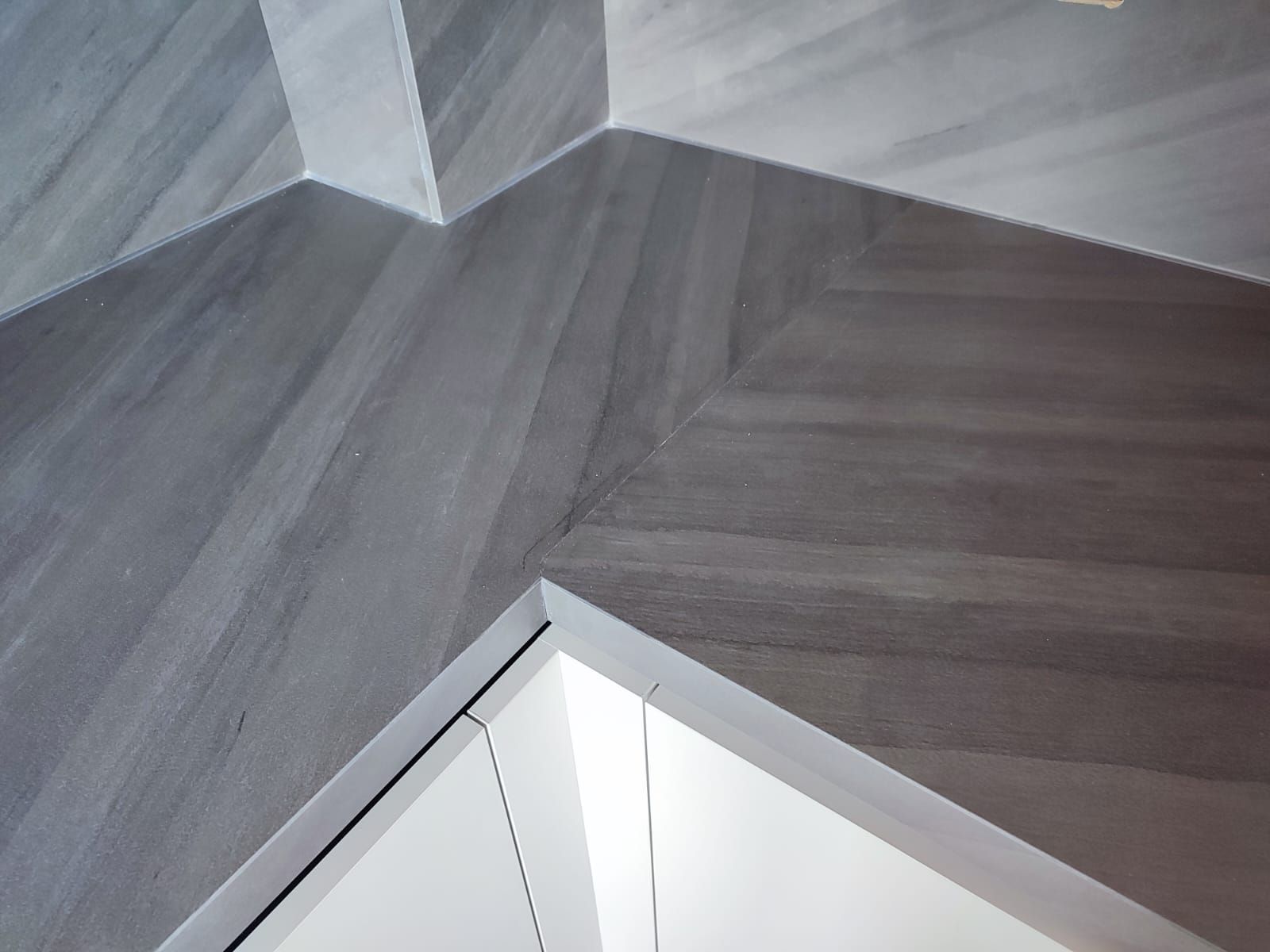 Pavimento piastrellato grigio con motivi geometrici; nella parte inferiore si trova uno stipite della porta bianco.