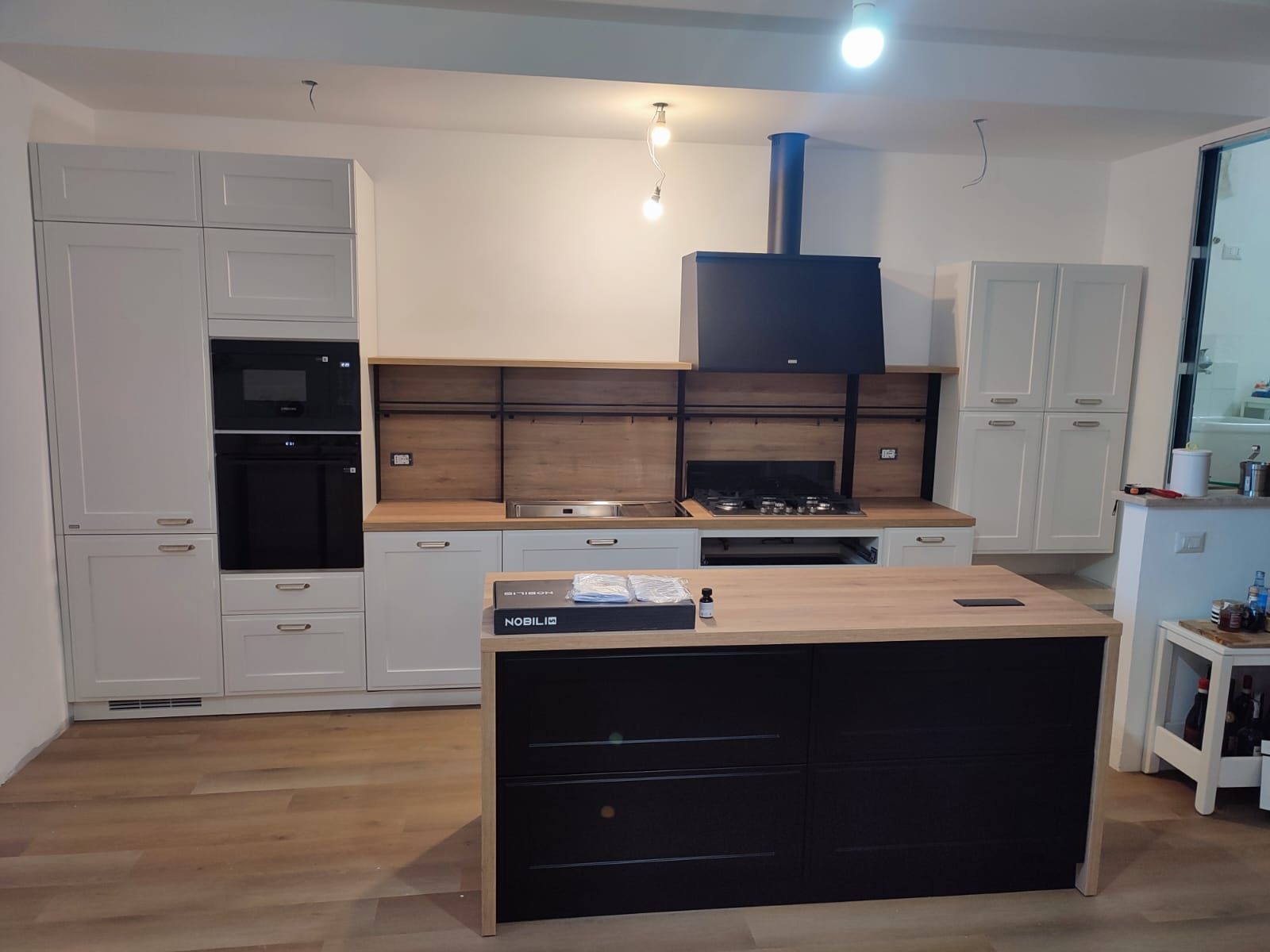 Cucina moderna con mobili bianchi, isola nera, dettagli in legno ed elettrodomestici.