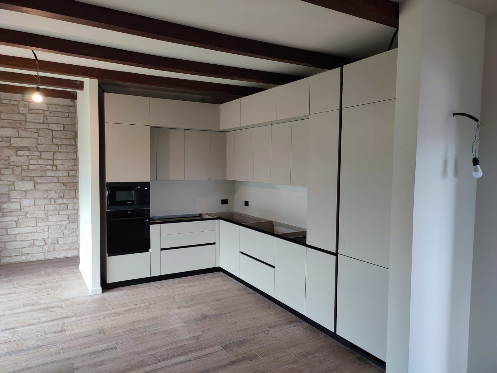 Mobili da cucina moderni bianchi con accenti neri in una stanza con travi in legno a vista e una parete in pietra.