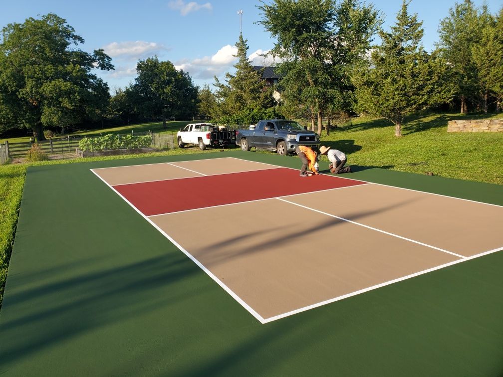 Two men are working on a tennis court with trees in the background