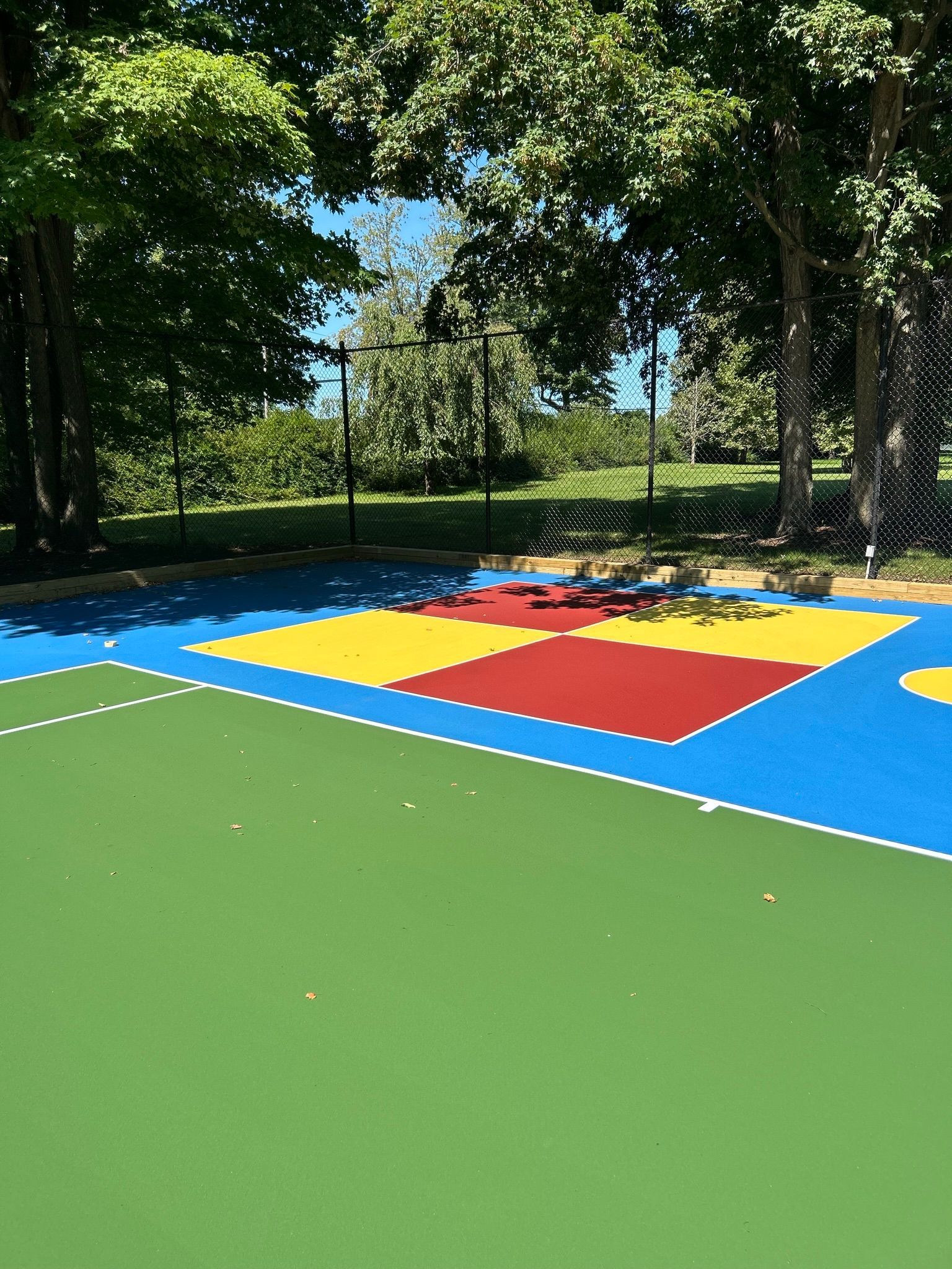 A colorful basketball court in a park with trees in the background