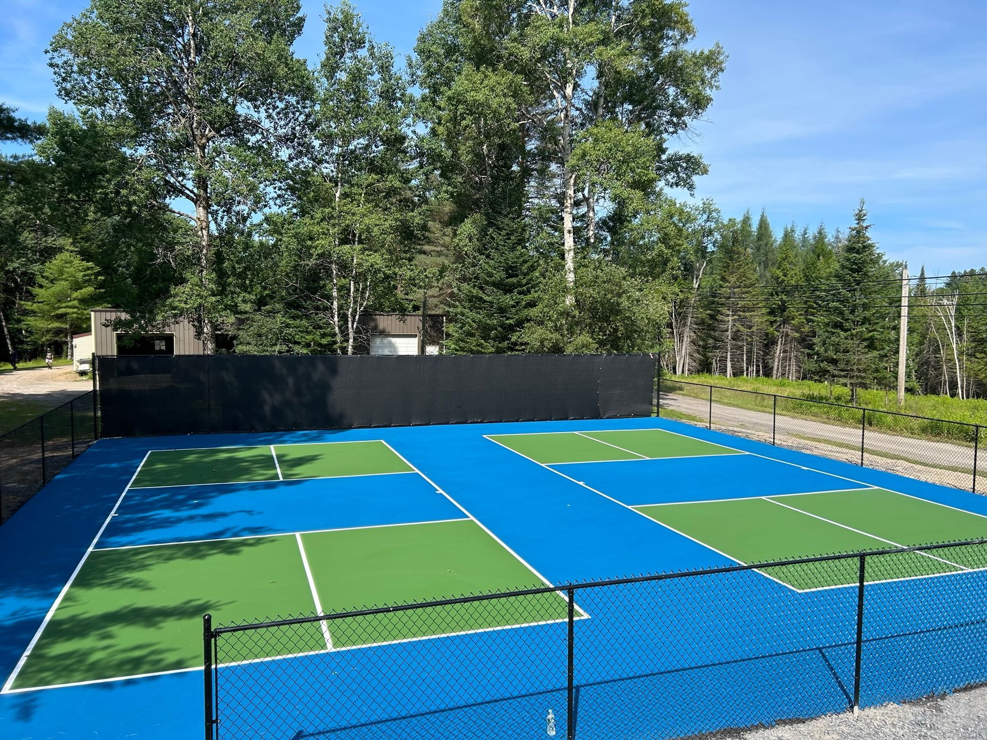A blue and green tennis court with trees in the background