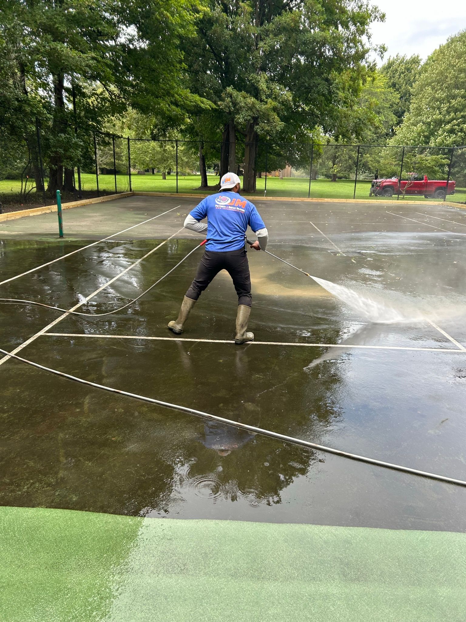 A man is cleaning a tennis court with a high pressure washer.