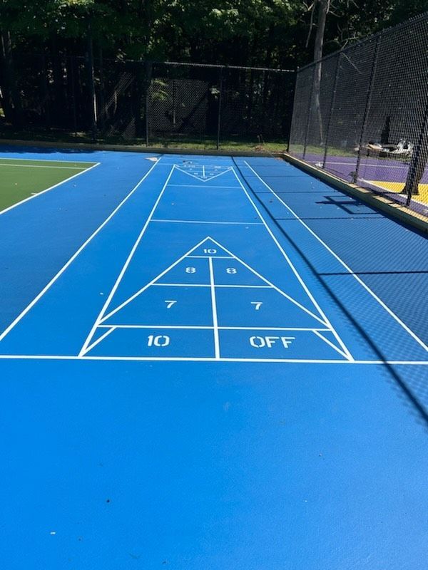 A blue tennis court has a shuffleboard court painted on it